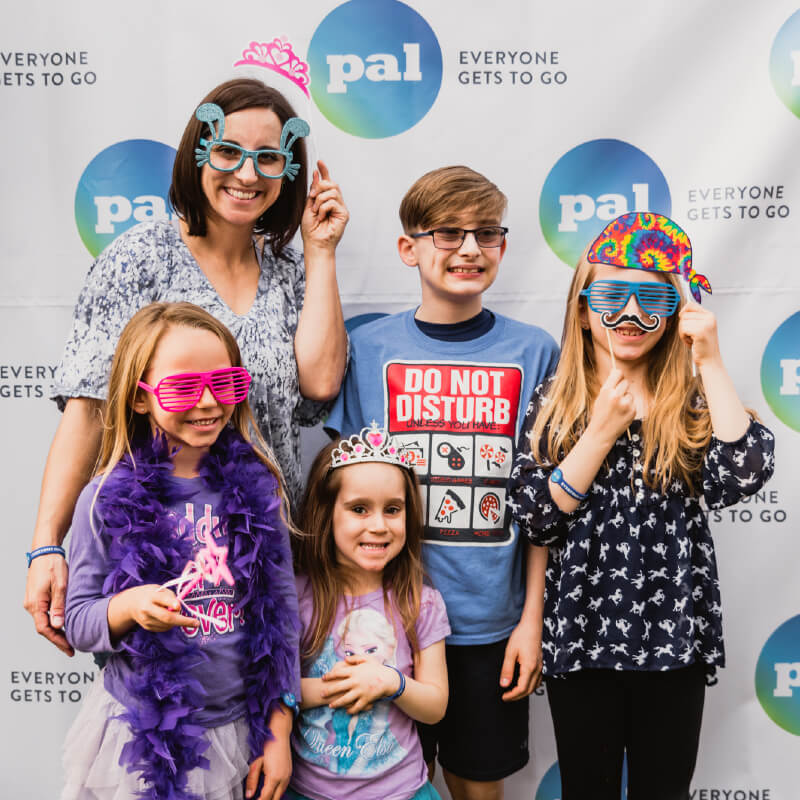 family with four children pose in a photobooth with silly props